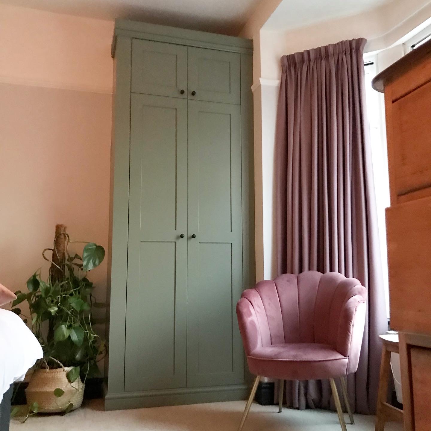 bedroom with fitted double wardrobe in sage green next to dusty pink armchair and plant