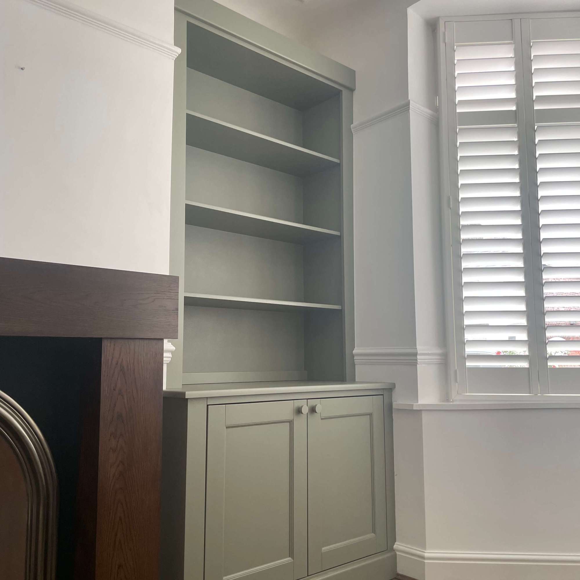 fitted olive alcove unit in living room with white shutters and fireplace